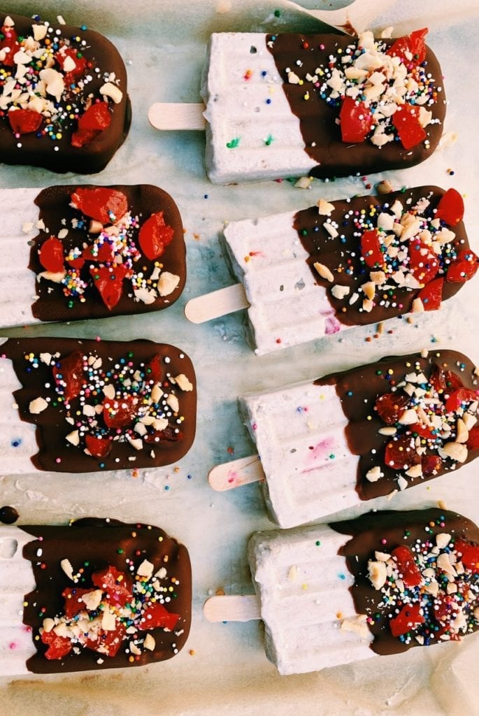 Overhead shot of banana split popsicles lined up on parchment paper. 