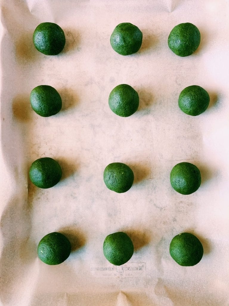 Parchment lined baking sheet with unbaked matcha shortbread balls on it. 