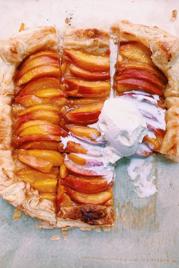 Baked nectarine tart cut into slices with ice cream on top.