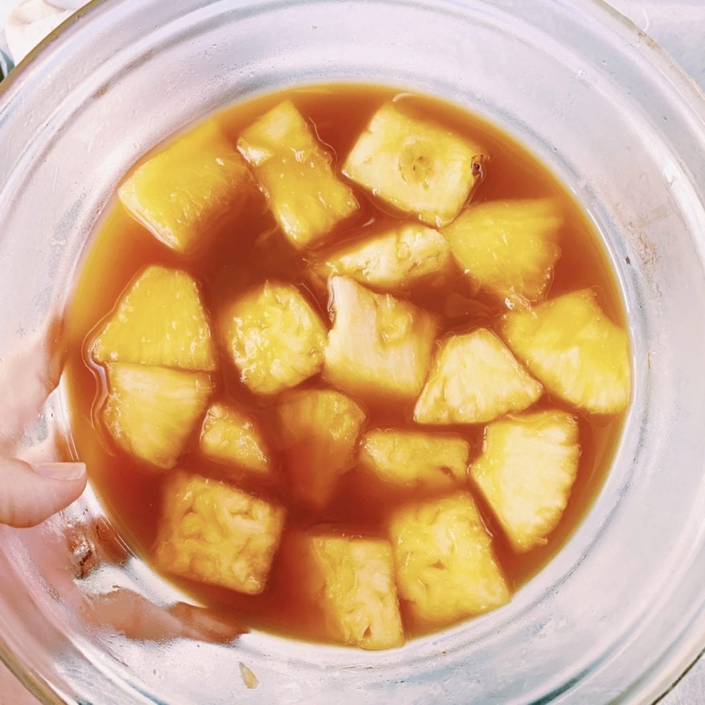 Pineapples marinating in a glass bowl to be used to make bacon wrapped pineapple bites  