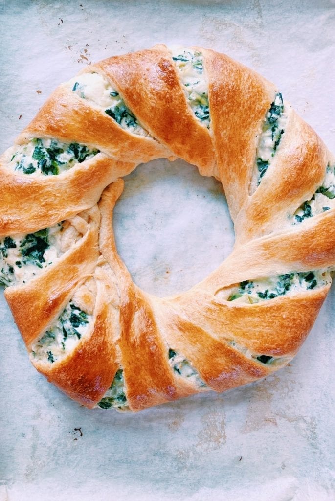 Overhead shot of spinach and artichoke dip crescent roll ring on parchment paper 