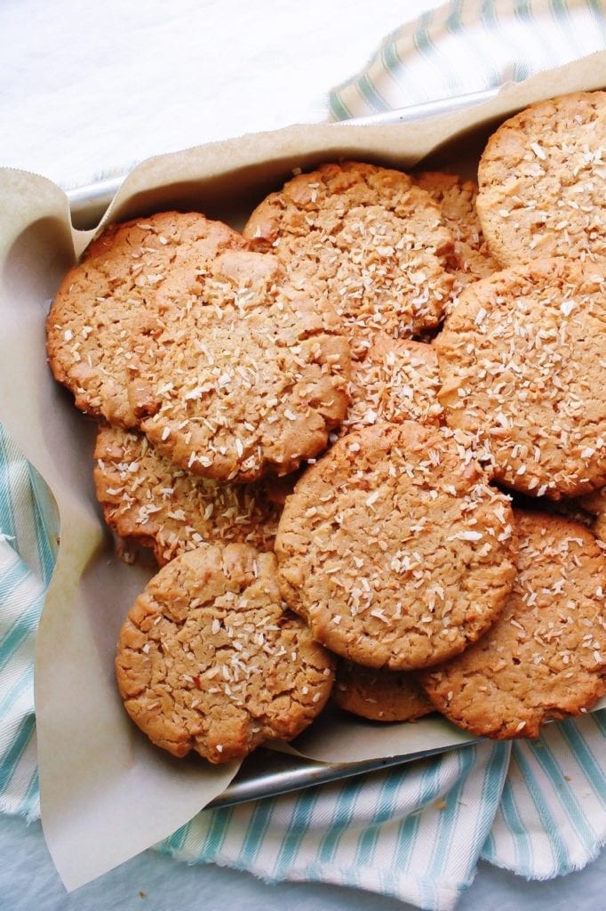 Peanut butter and toasted coconut cookies stack on a parchment lined baking sheet