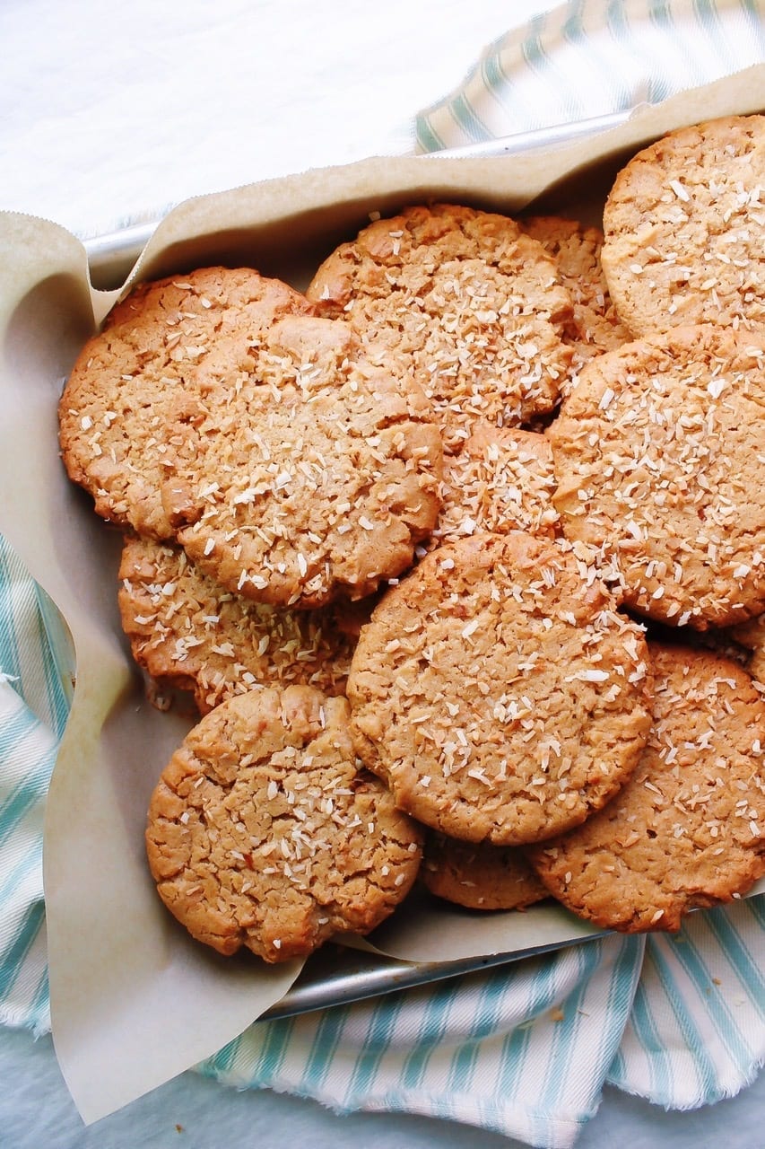 Peanut butter and toasted coconut cookies stacked on a parchment lined baking sheet