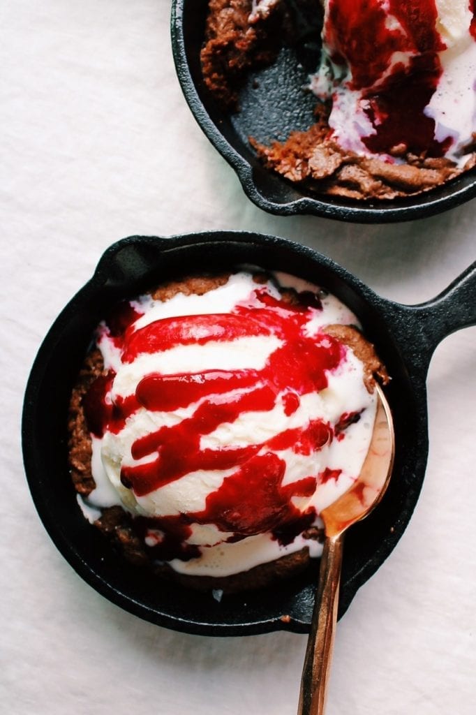 Double chocolate chunk skillet cookies topped with vanilla ice cream and raspberry sauce 