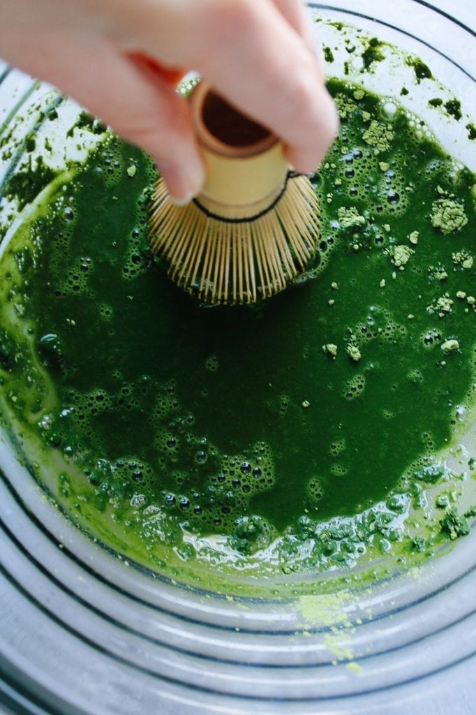 Hand using a matcha whisk to blend matcha powder and water