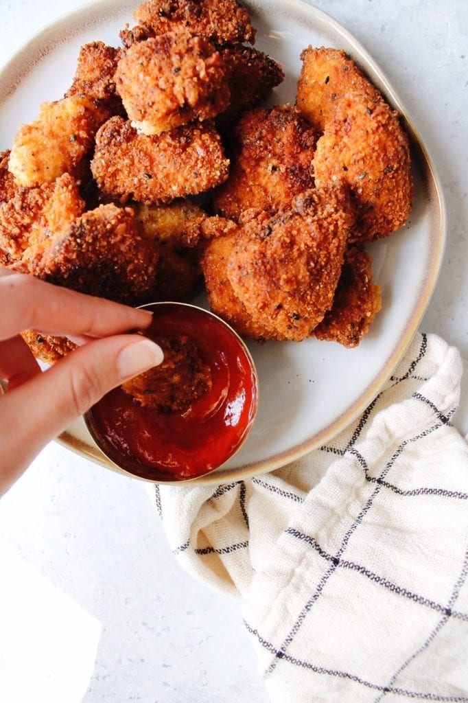 A hand dipping a cracker crusted chicken nugget into a little dish with ketchup.