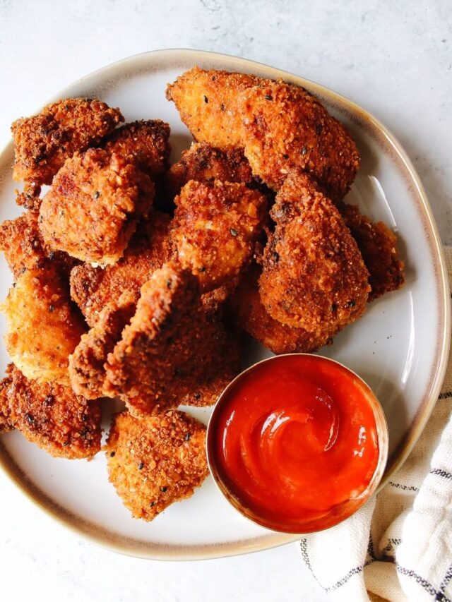 Homemade chicken nuggets on a white plate with ketchup