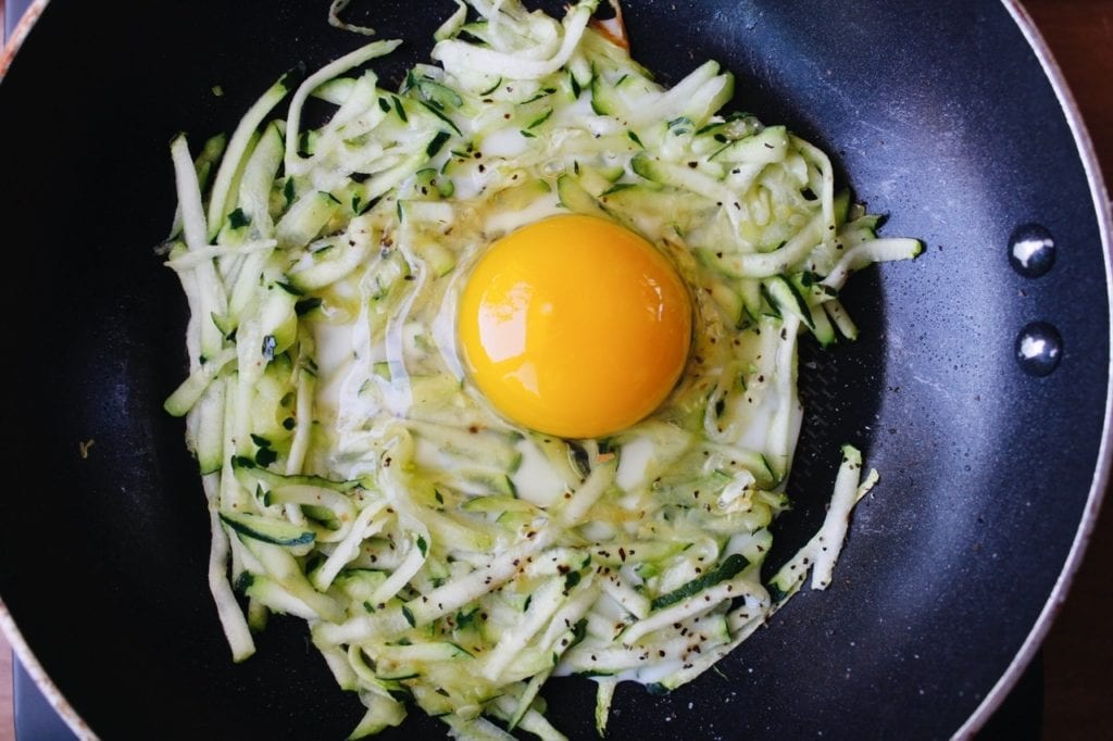 egg on top of shredded zucchini in a pan
