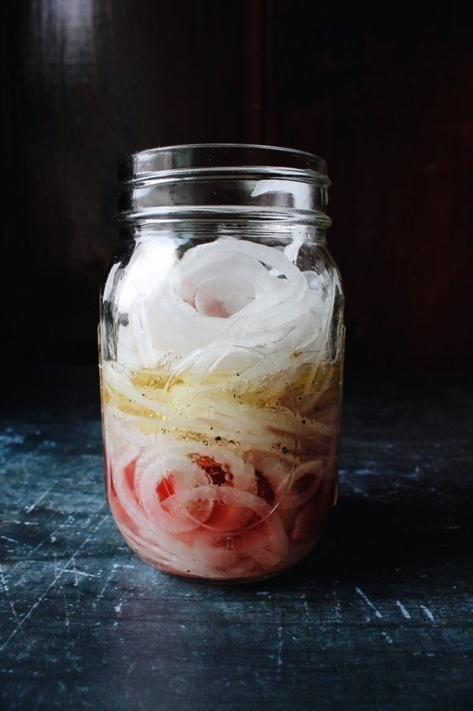 side view of marinated onions in a clear glass jar