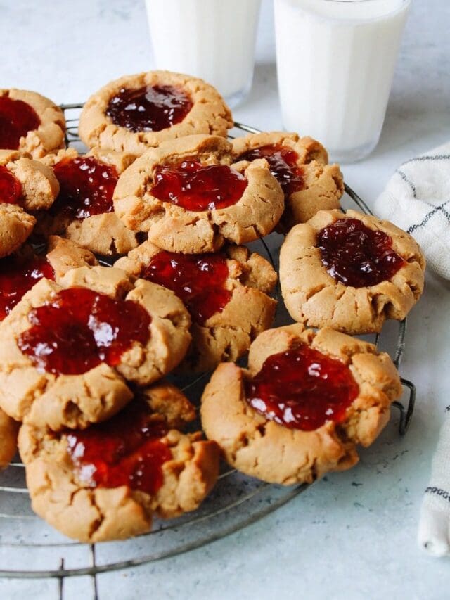 peanut butter and jelly cookies stacked on a cooling rack with two glasses of milk