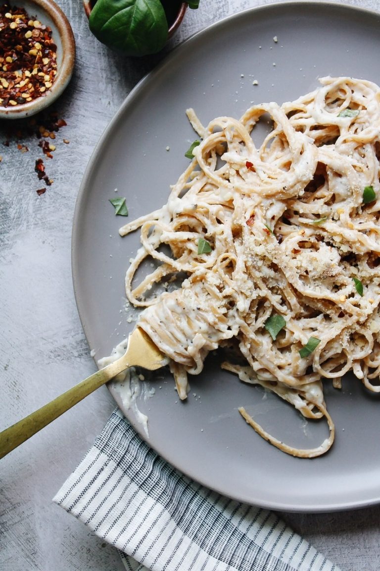 Fettuccini alfredo on a gray plate topped with basil and pepper flakes