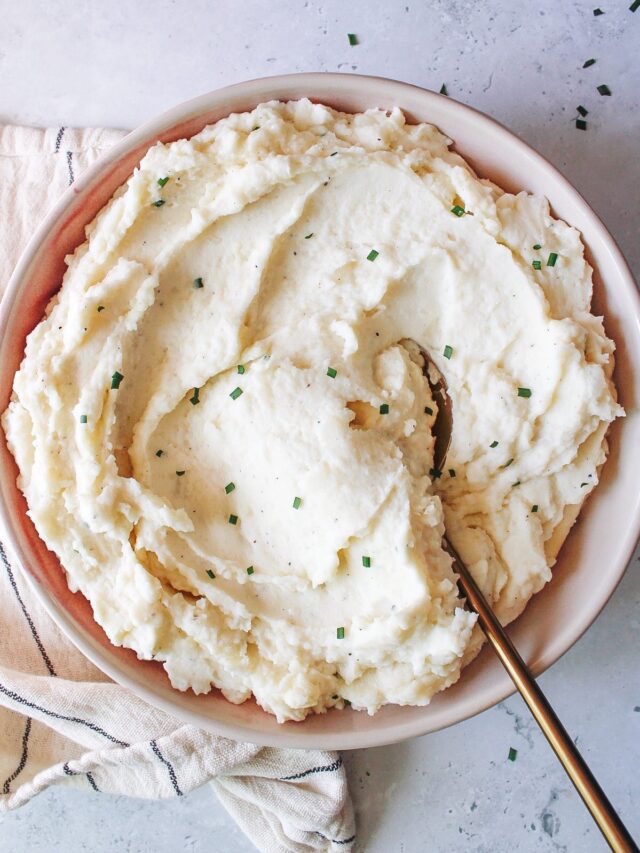 cream cheese and chive mashed potatoes in a large bowl with a gold serving spoon