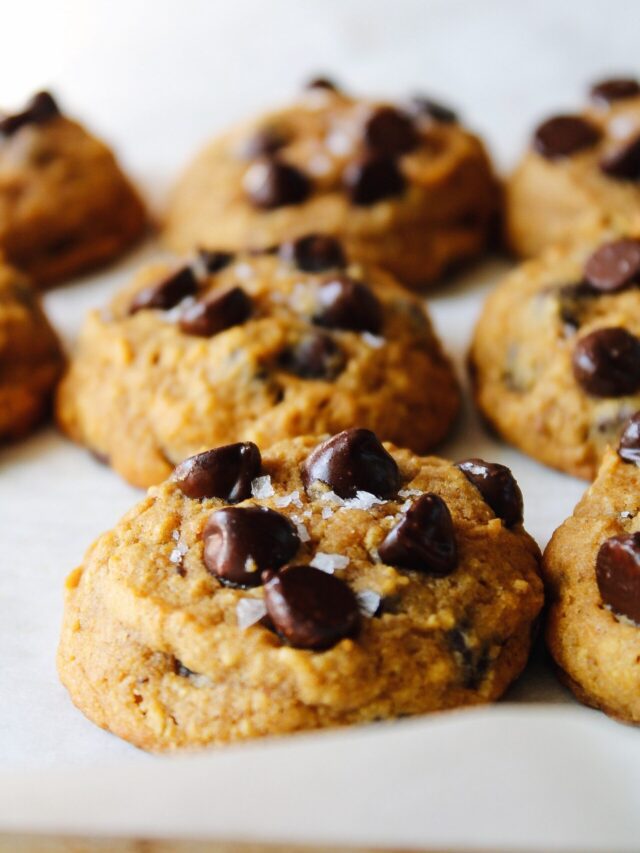 gluten-free pumpkin chocolate chip cookies on a baking sheet lined with white parchment paper. Cookies are topped with sea salt.