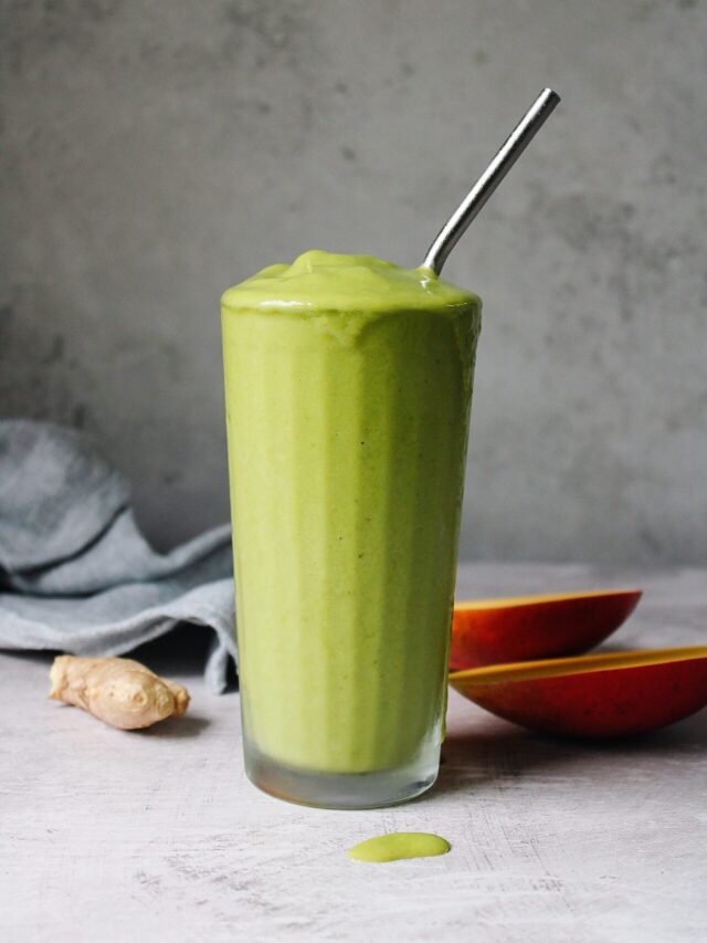 oat milk tropical green smoothie in a clear glass with a metal straw