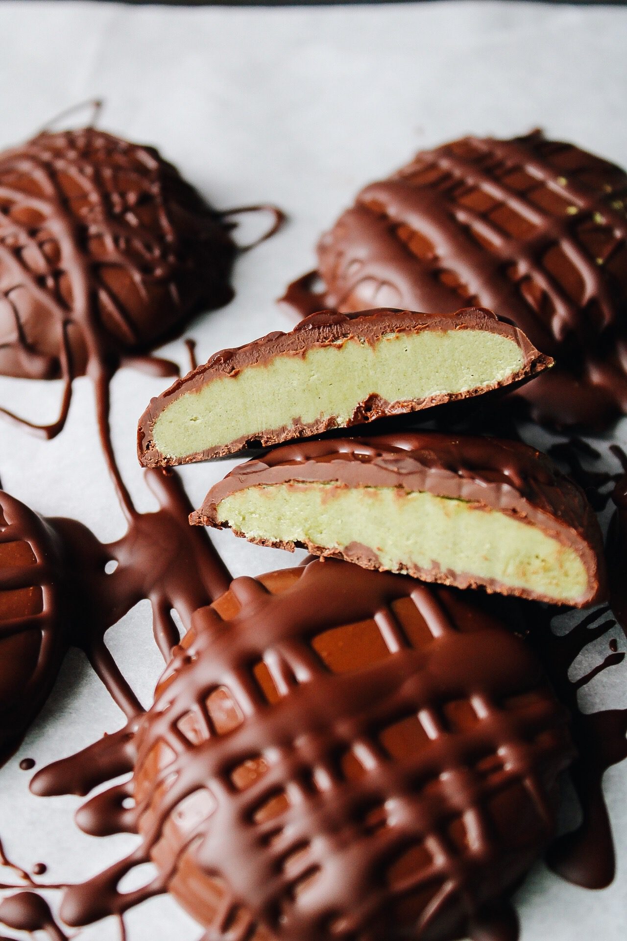 matcha cream chocolate truffles on parchment, one is cut in half to show the creamy matcha center