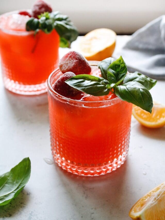 strawberry basil lemonade in two clear glasses topped with basil and frozen strawberries