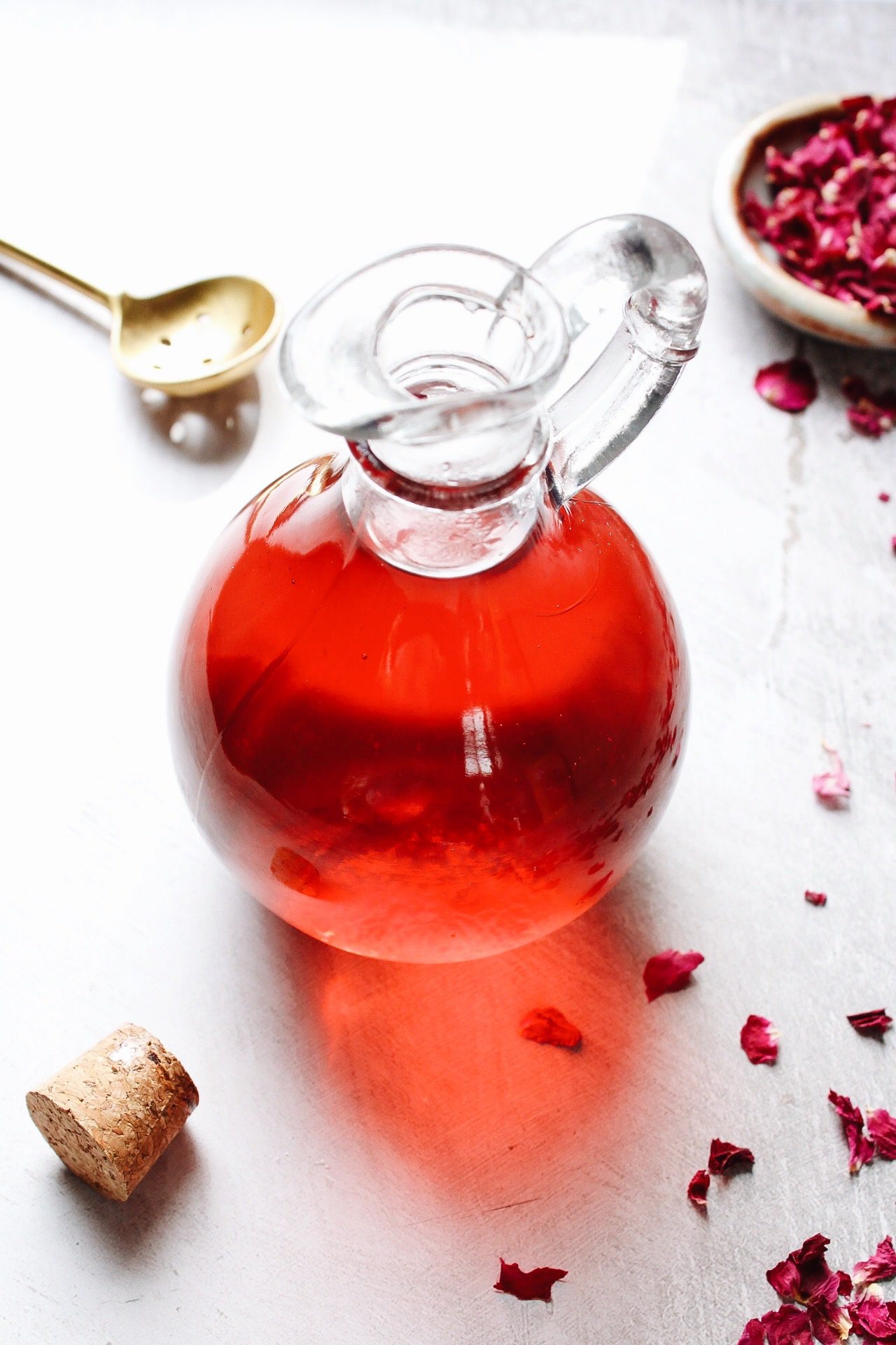 rose simple syrup in a glass jar with rose petals scattered around