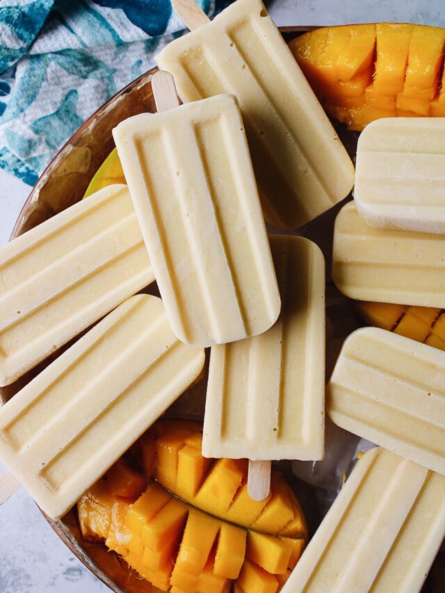 mango popsicles on a bowl of ice with cut mango scattered around