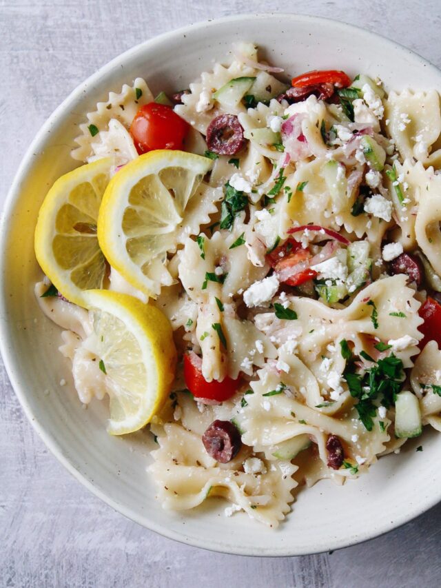 close up of mediterranean pasta salad in a white bowl topped with lemons