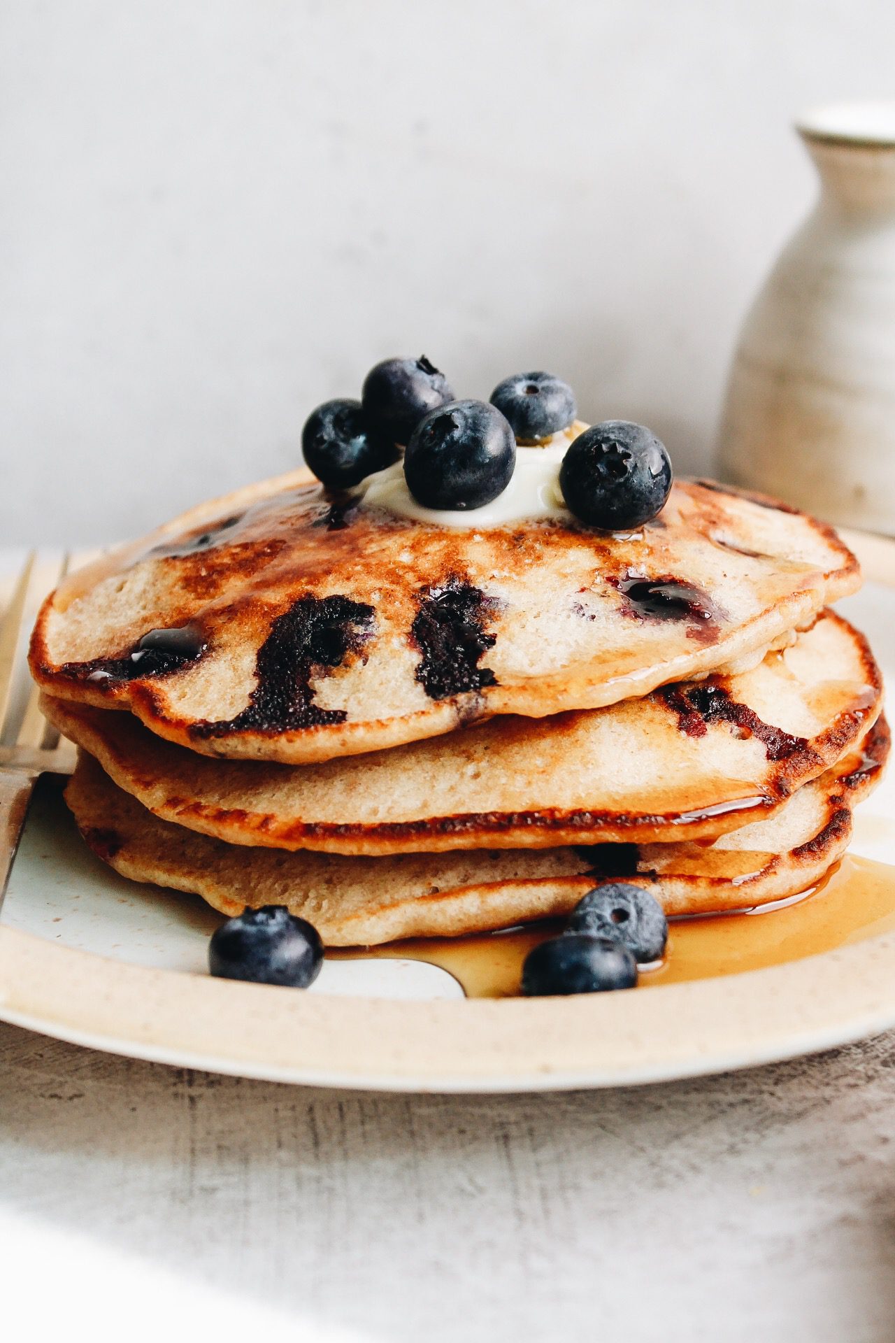 stack of blueberry lemon pancakes on a white plate topped with blueberries and syrup