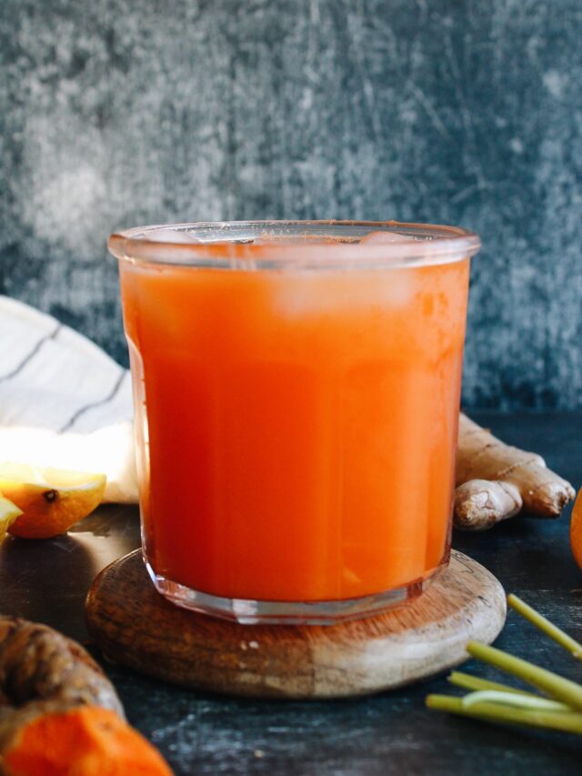 carrot ginger turmeric juice in a clear glass on a wooden coaster