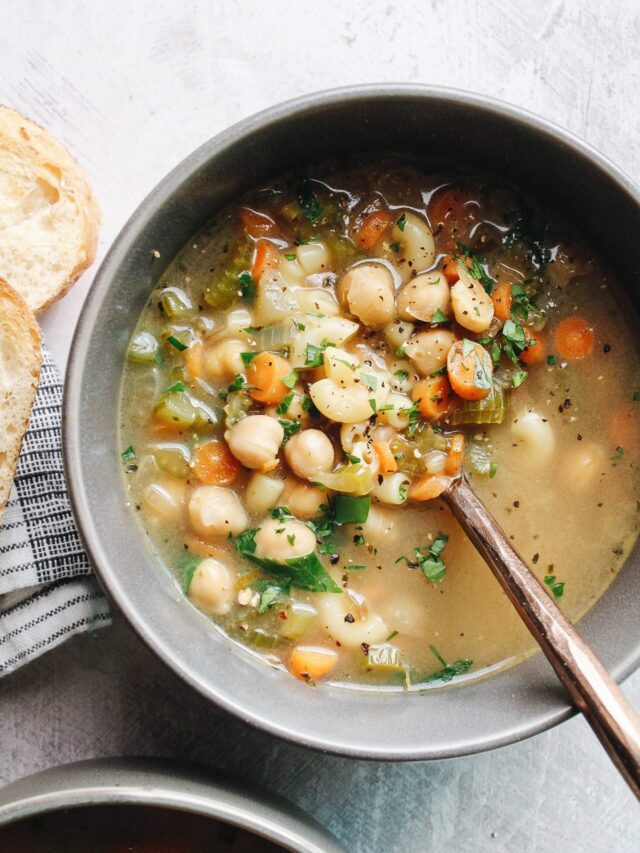 chickpea noodle soup in a gray bowl next to bread