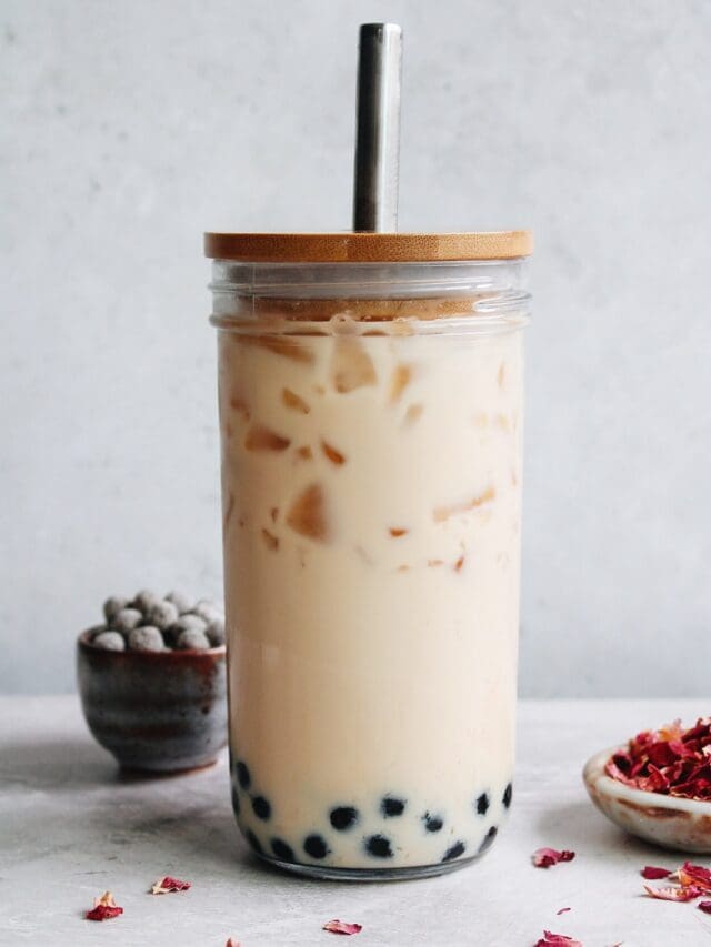 rose milk tea in a boba glass with rose petals and tapioca pearls scattered around