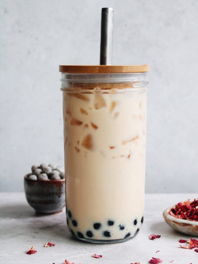 rose milk tea in a boba glass with rose petals and tapioca pearls scattered around