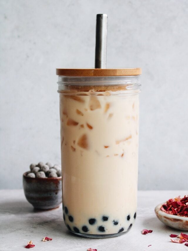 rose milk tea in a boba glass with rose petals and tapioca pearls scattered around