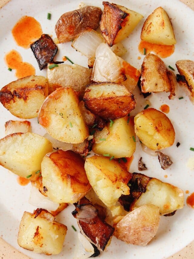 skillet fried breakfast potatoes on a plate with hot sauce and chives