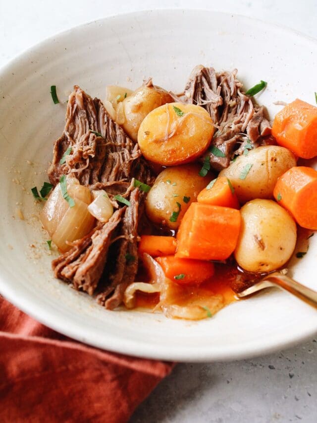 dutch oven pot roast in a white bowl with a golden fork