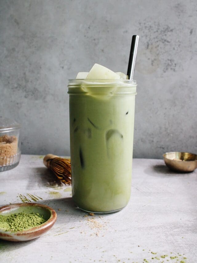 oat milk matcha latte in a clear glass with a metal straw