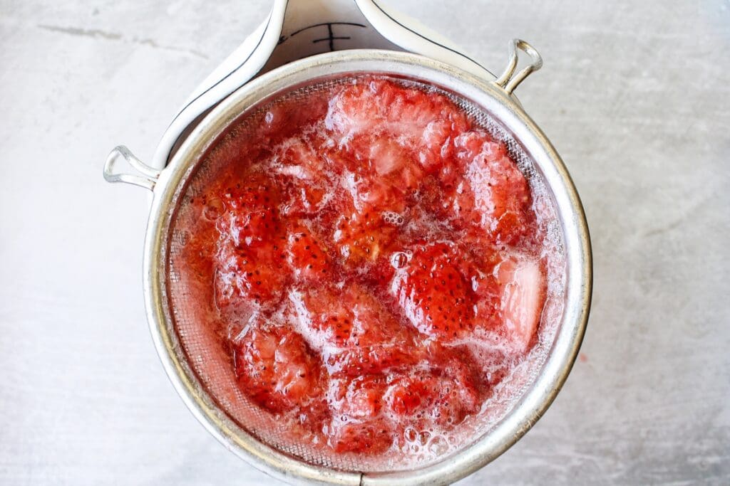 strawberry syrup being strained through a mesh sieve