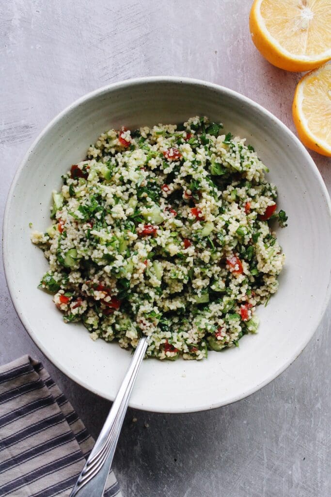 couscous tabbouleh in a white bowl with a serving spoon