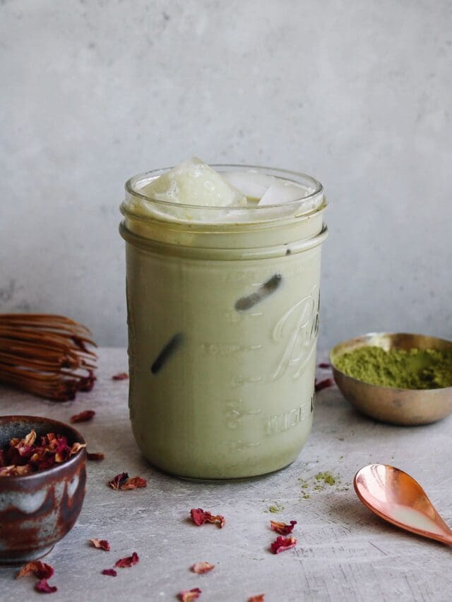 rose matcha latte in a glass jar with dried rose petals scattered around