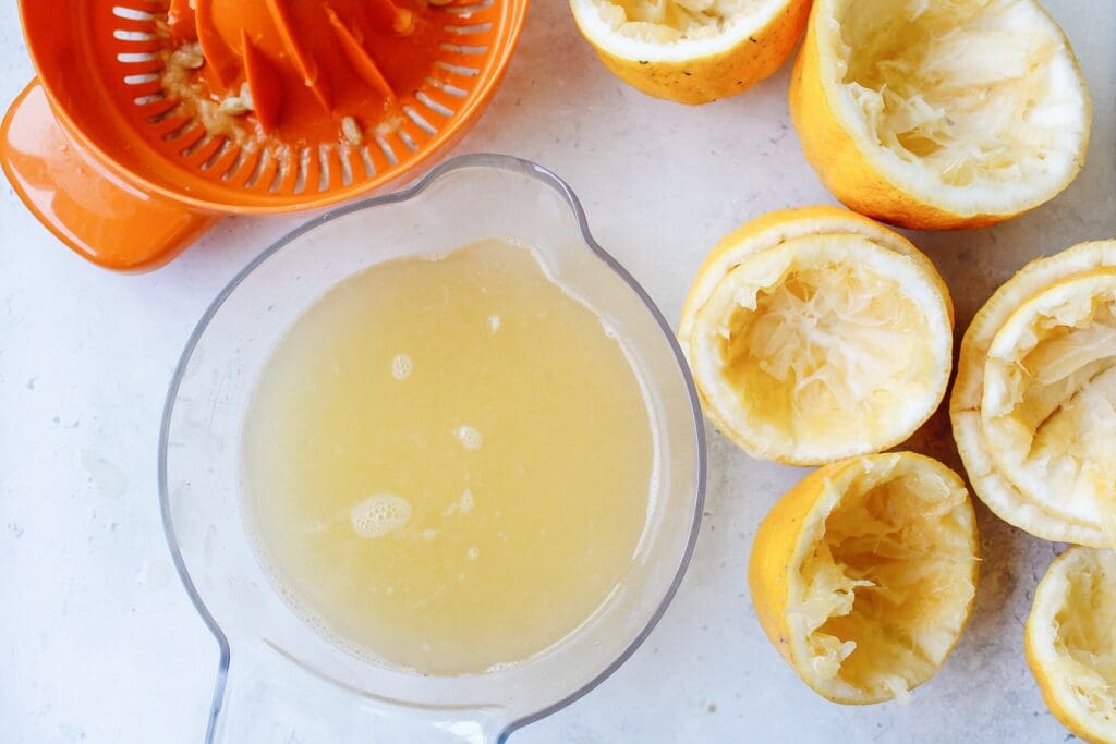 fresh lemon juice in a citrus juice next to juiced lemons