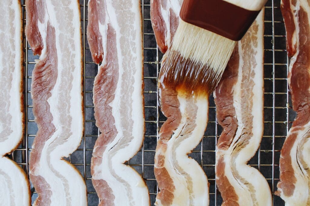 a pastry brush brushing maple syrup over bacon