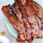 maple bacon on a green plate with drops of maple syrup next to it