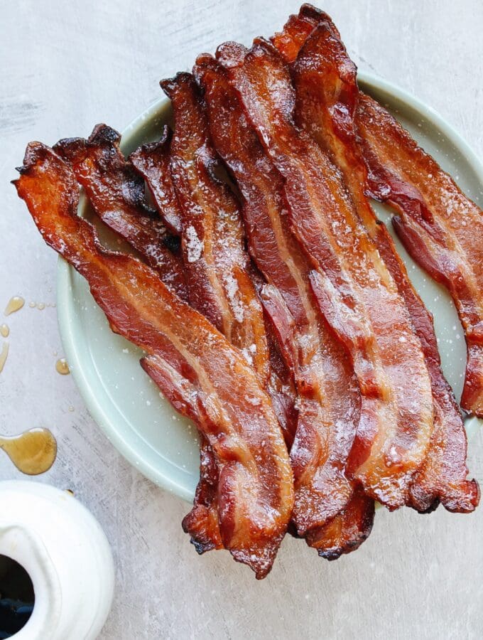 maple bacon on a green plate with drops of maple syrup next to it