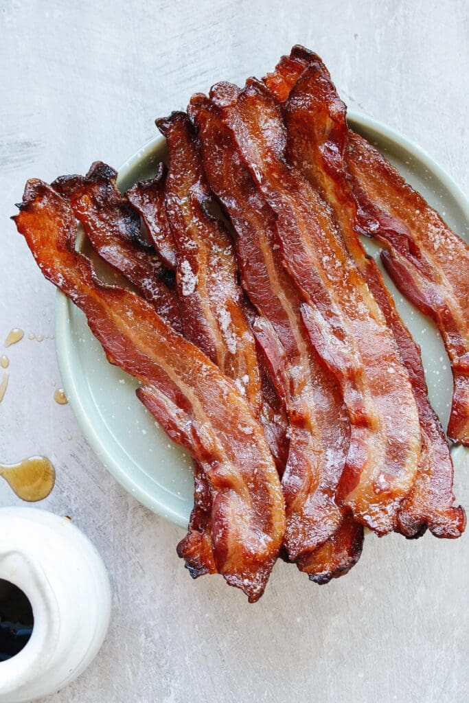 maple bacon on a green plate with drops of maple syrup next to it