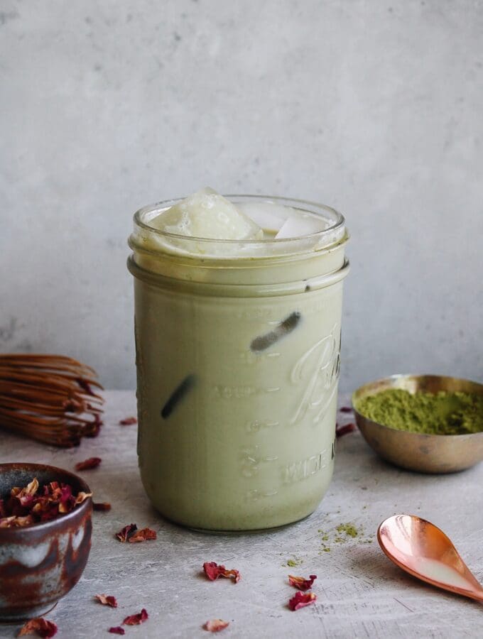 rose matcha latte in a glass jar with dried rose petals scattered around