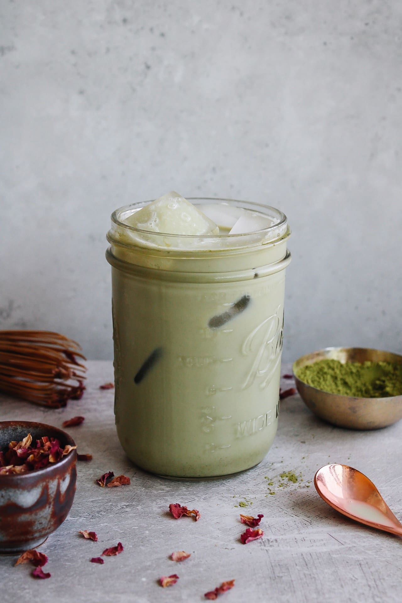 rose matcha latte in a glass jar surrounded by rose petals