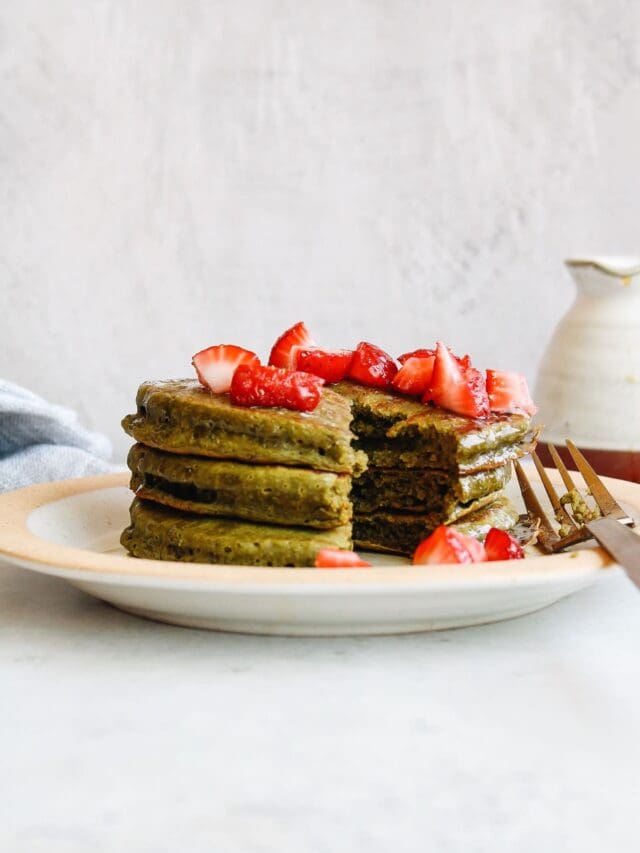 three matcha pancakes on a plate topped with fresh strawberries