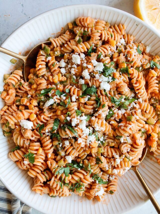 spicy pasta salad in a large white bowl with gold serving spoons