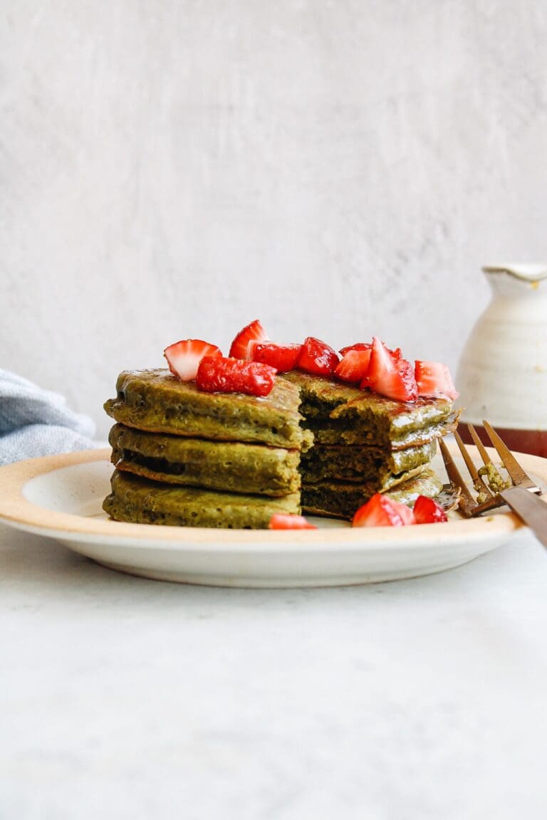 three matcha pancakes on a plate topped with fresh strawberries