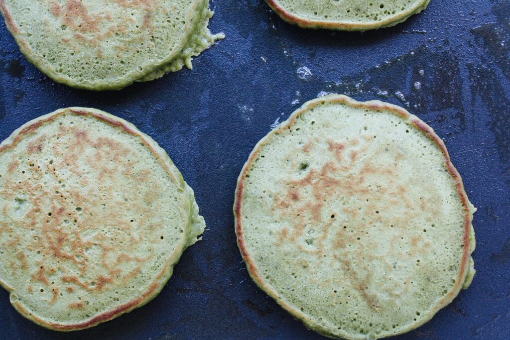 matcha pancakes on a griddle after being flipped