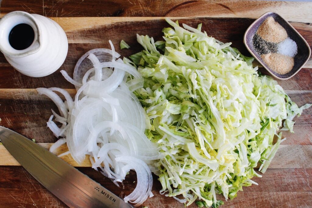 thinly sliced iceberg lettuce and onions on a wooden cutting board