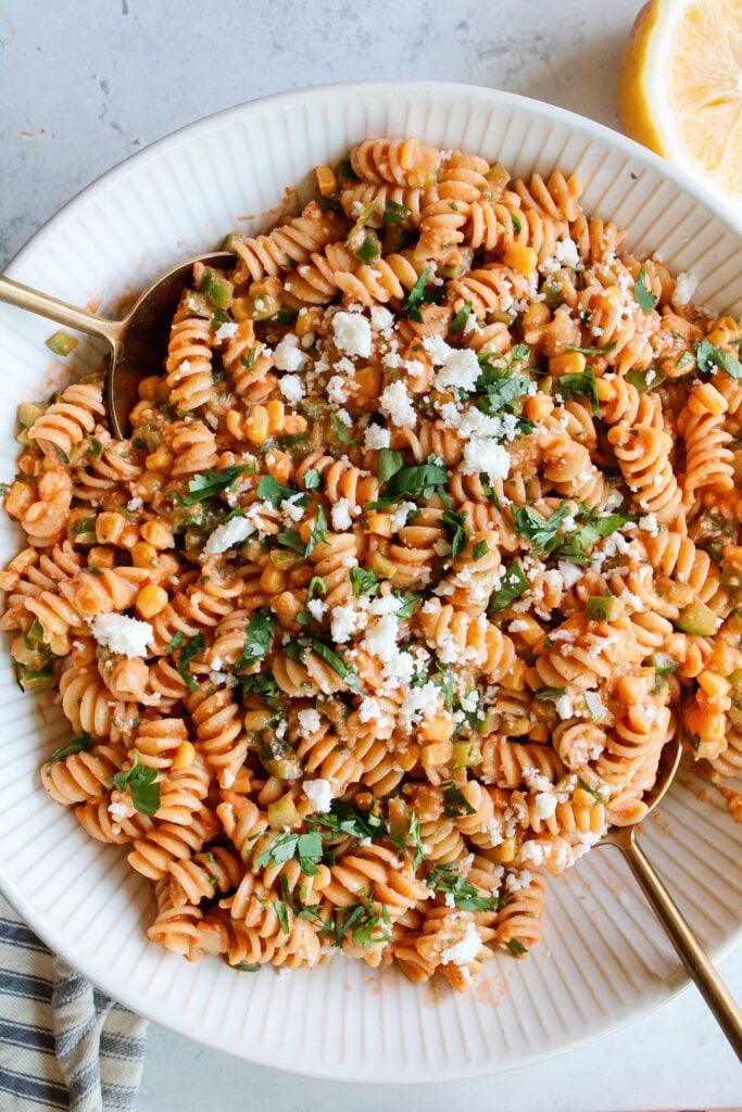 spicy pasta salad in a large white bowl with gold serving spoons