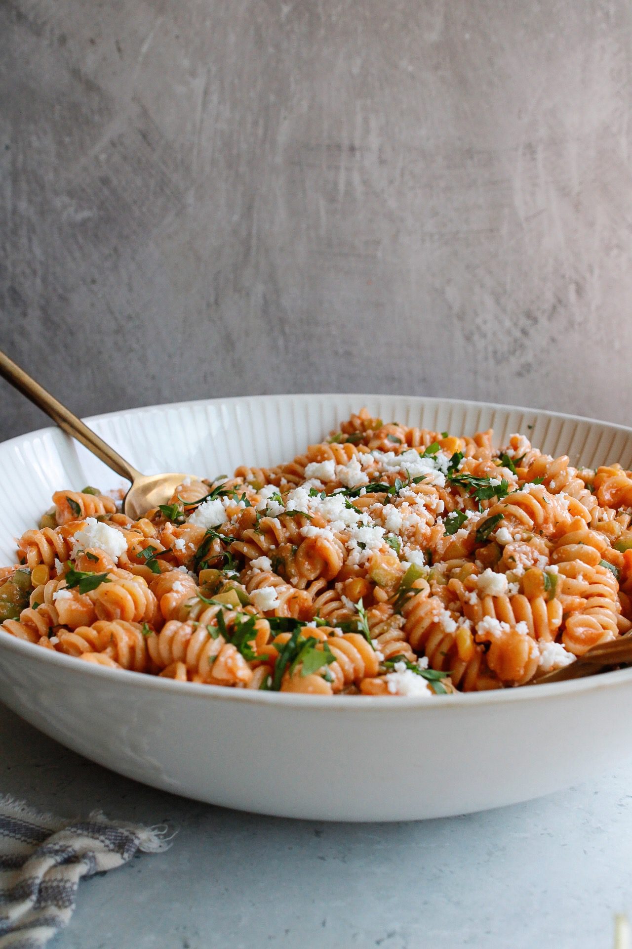 spicy pasta salad with cilantro, cotija and corn in a white bowl with a gold serving spoon
