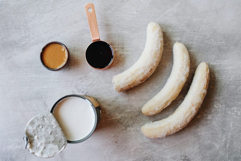 frozen bananas, peanut butter, maple syrup and coconut milk on a gray background